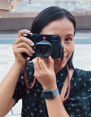 Woman holding a black compact camera in front of her face, looking at the lens