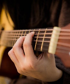 A musician’s hand pressing the strings of an acoustic guitar neck