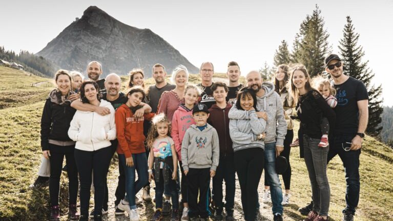 Multigenerational family group posing together in front of a sunny mountain peak