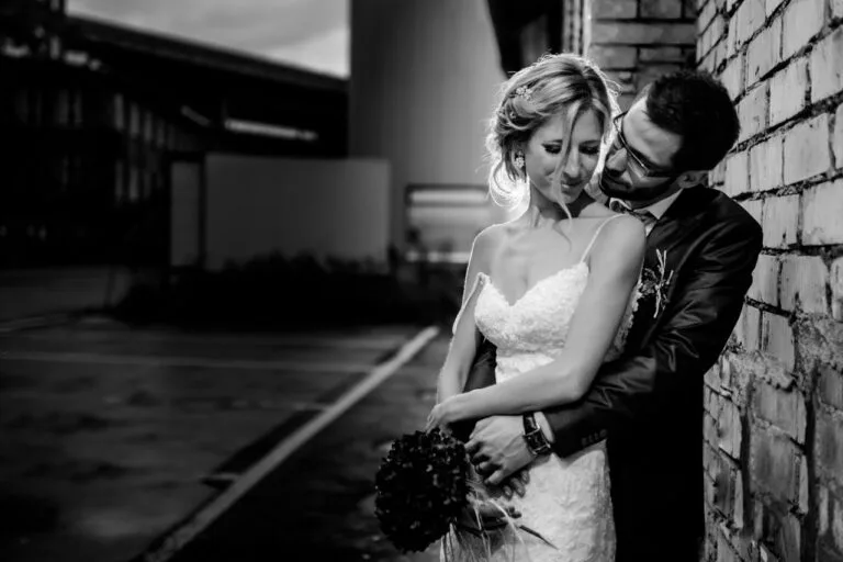 Couple en noir et blanc, l'homme enlace la femme contre un mur