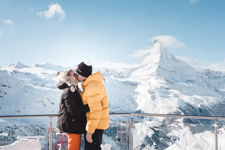 Couple s'embrassant sur un balcon enneigé devant un sommet montagneux pyramidal