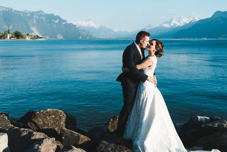 Couple en tenue de cérémonie s'embrassant sur un rivage rocheux face au lac