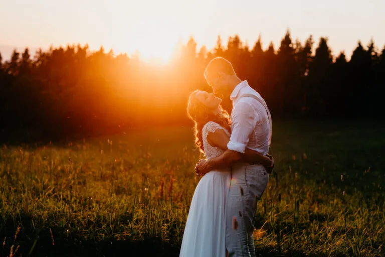 Couple enlacé dans un champ d'herbes hautes sous un soleil couchant