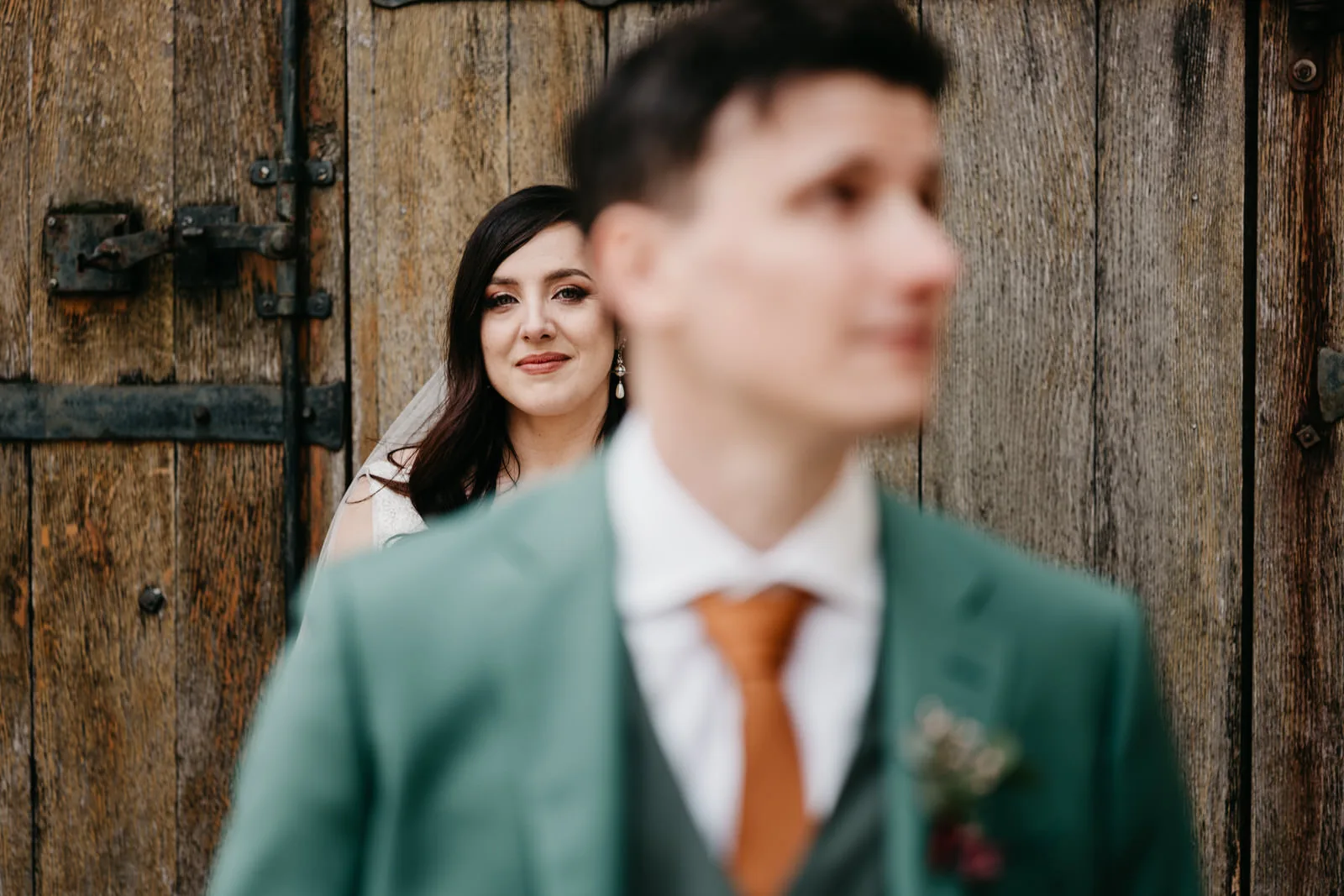 Femme au regard doux devant une porte en bois massif et ferrures