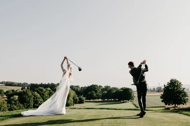 Une mariée en robe blanche et un marié en costume sombre jouent au golf